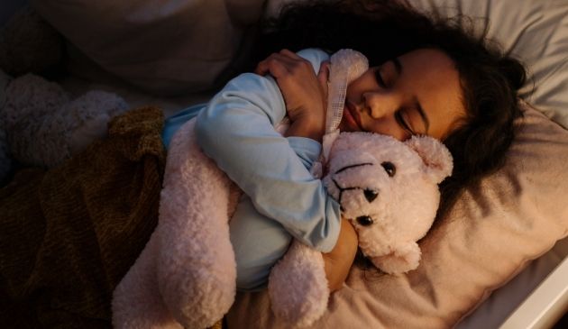 child asleep in bed hugging teddy bear