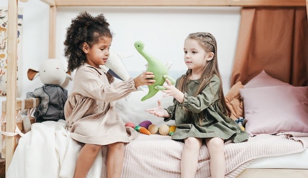 Children playing with dinosaur toy on bed