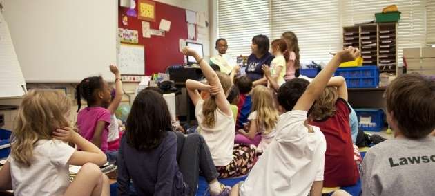Children in a classroom with hands up