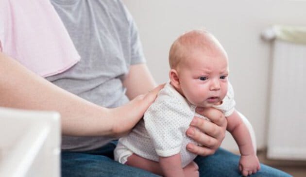 Adult supporting baby on lap with one hand on its over chest and one on back